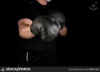 young man stands in a boxing rack, wearing very old vintage black boxing gloves on his hands, dark background