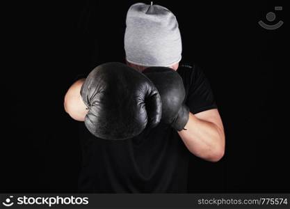 young man stands in a boxing rack, wearing very old vintage brown boxing gloves on his hands, black background