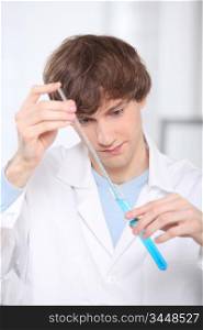 Young man stirring blue liquid in a test tube