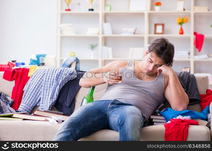 Young man student drunk drinking alcohol in a messy room