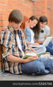 Young man studying book college friends sitting ground using laptop