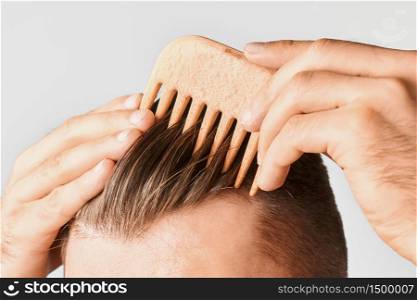 Young man styling his hair with a wooden comb. Hair styling at home. Advertising concept of shampoo for healthy hair and against dandruff. Young man styling his hair with a wooden comb. Hair styling at home. Advertising concept of shampoo for healthy hair and against dandruff.