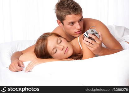 Young man suprised by alarm clock in white bed