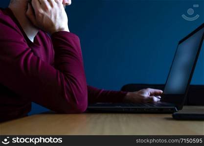 Young man surfs the internet on his laptop late at night with blue background, working late with moody colors blue and red dark. Young man surfs the internet on his laptop late at night with blue background, working late with moody colors blue and red