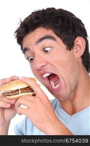 Young man taking an exaggerated bite out of a hamburger