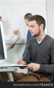 Young man taking notes form computer