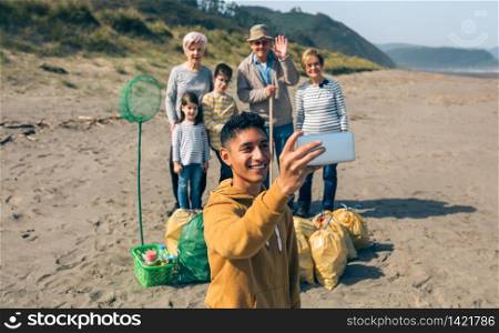 Young man taking selfie with mobile to group of volunteers after cleaning the beach. Selective focus on guy in foreground. Young man taking selfie to group of volunteers after cleaning beach