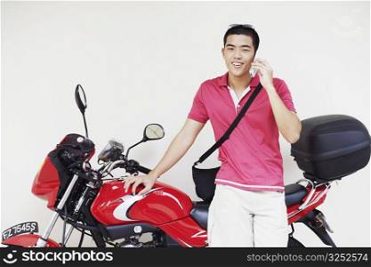 Young man talking on a mobile phone and leaning against a motorcycle