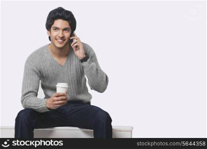Young man talking on cell phone while holding disposable cup