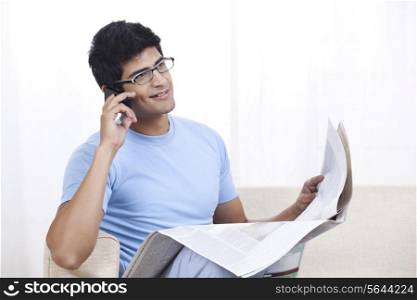Young man talking on mobile phone with newspaper