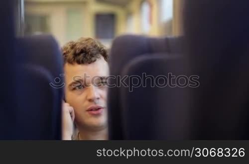 Young man talking on the phone in moving train. View between seats.