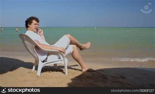 Young man talking on the phone while sunbathing on the beach