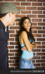 Young man talking to young woman standing in front of brick wall