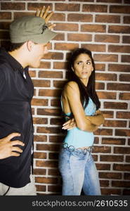 Young man talking to young woman standing in front of brick wall