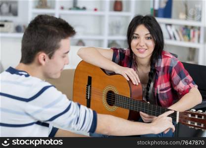 young man teaches his girlfriend to play the guitar indoors