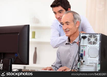 Young man teaching an elderly man computer skills