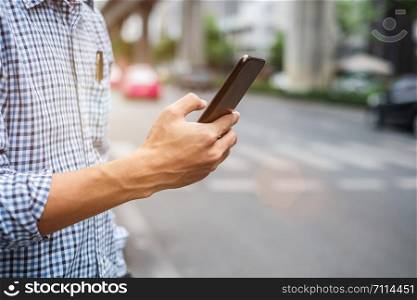 Young man tourist or casual businessman ordering taxi via cab application on smartphone in city street, Male traveler using mobile phone and Searching direction on digital map at Bangkok, Thailand