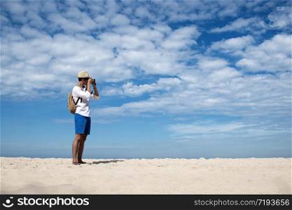 Young man travel outdoor on tropical beach with blue sky and white cloud using DSLR professional camera take a photo on vacation time with love nature. Outdoor travel lifestyle concept.