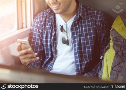Young man traveler with backpack and hat use phone with waiting for train. Travel concept.