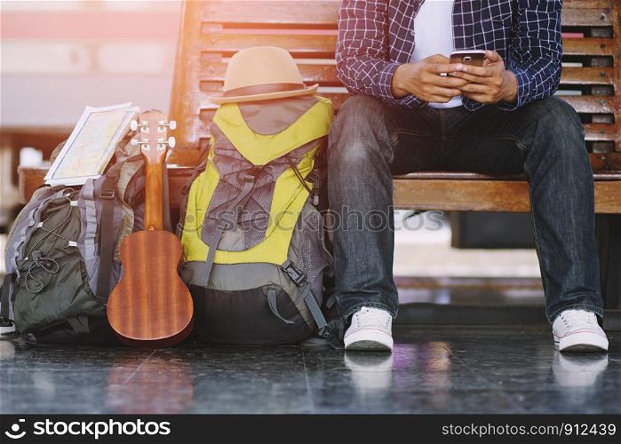 Young man traveler with backpack and Travel equipment sit use phone with waiting for train. Travel concept.