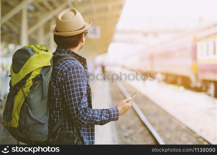 Young man traveler with Wearing sunglasses backpack and hat looking the map with waiting for train. Travel concept.