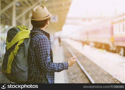 Young man traveler with Wearing sunglasses backpack and hat looking the map with waiting for train. Travel concept.