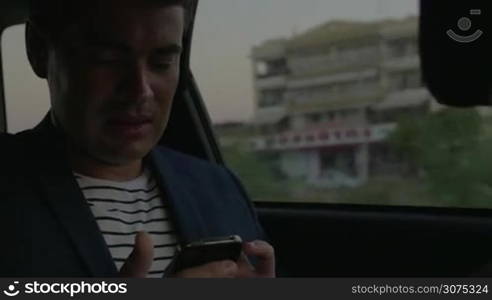Young man traveling by car in the city. He using smart phone and looking out the window