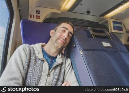Young man traveling on a train and sleep on blue suitcase next to him.