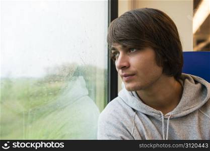 Young Man Travelling In Train, Looking Out Of Window