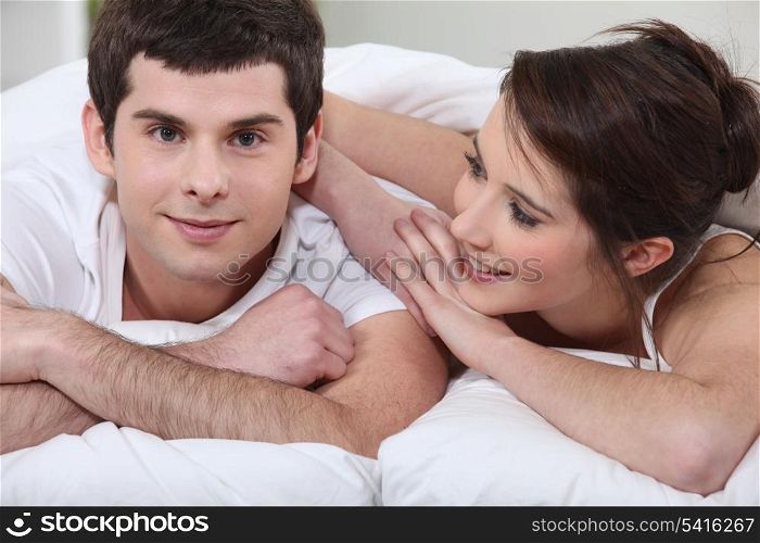 young man turned toward camera with girlfriend in bed