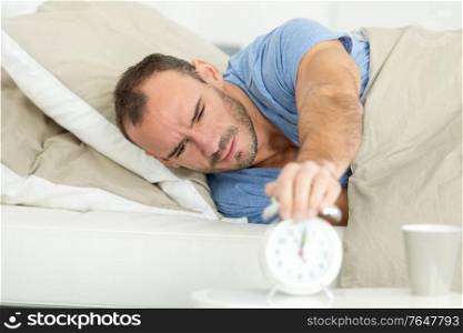 young man turning off the alarm clock on the bed