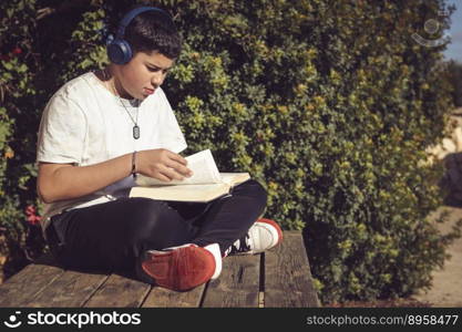 young man turning the pages of the book he is reading, sitting on the wooden bench in the garden of the country house, on the outskirts of the city,. young man turning the pages of the book he is reading