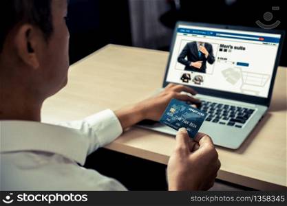 Young man use credit card for shopping payment online on laptop computer application or website. E-commerce and online shopping concept.