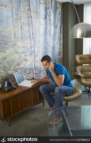 Young man using a laptop and talking on a mobile phone