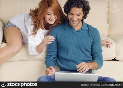 Young man using a laptop with a young woman leaning over him