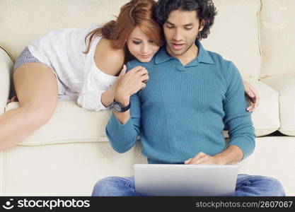 Young man using a laptop with a young woman leaning over him