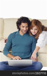 Young man using a laptop with a young woman leaning over him