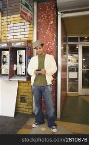 Young man using a mobile phone near a pay phone