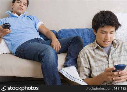 Young man using a mobile phone while another young man operating a remote control