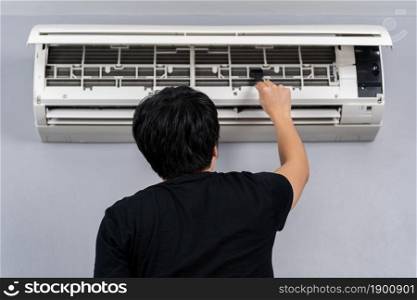 young man using brush to cleaning the air conditioner indoors at hone