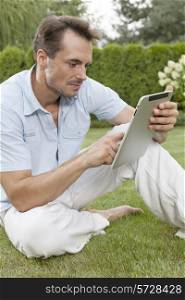 Young man using digital tablet while sitting on grass in park
