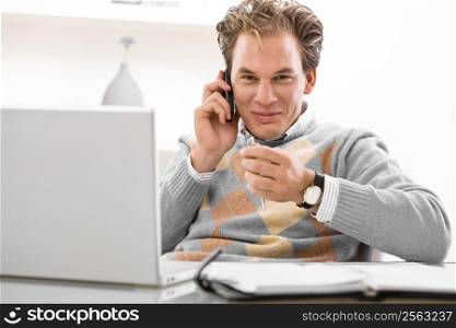 Young man using laptop and calling on phone at home.