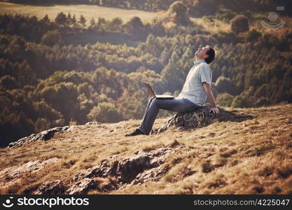 young man using laptop sitting on the grass on the hillside