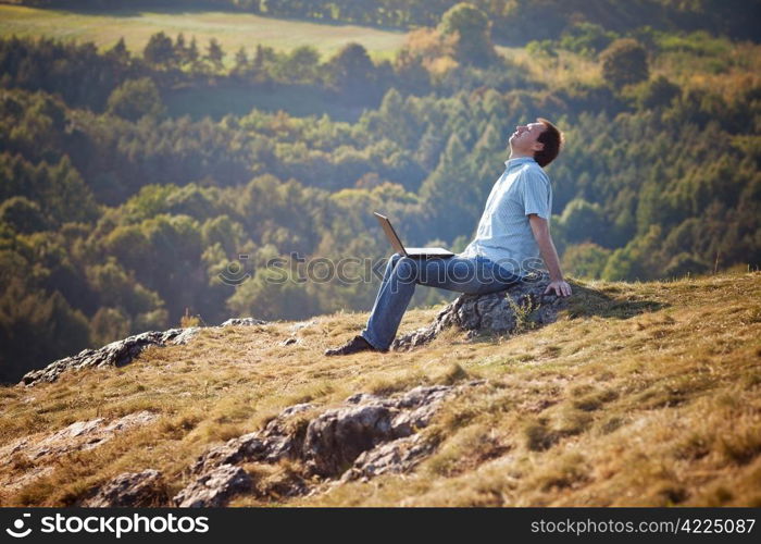 young man using laptop sitting on the grass on the hillside