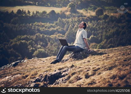 young man using laptop sitting on the grass on the hillside