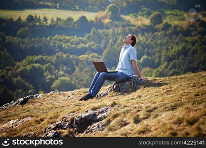 young man using laptop sitting on the grass on the hillside