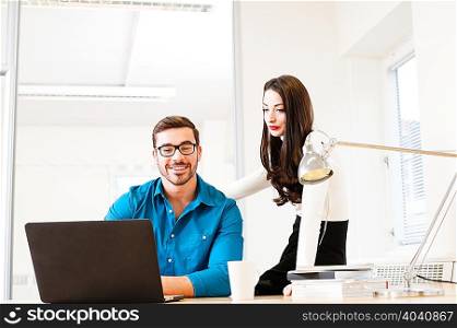 Young man using laptop with female colleague