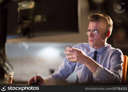 Young man using mobile phone while working on computer at night in dark office.