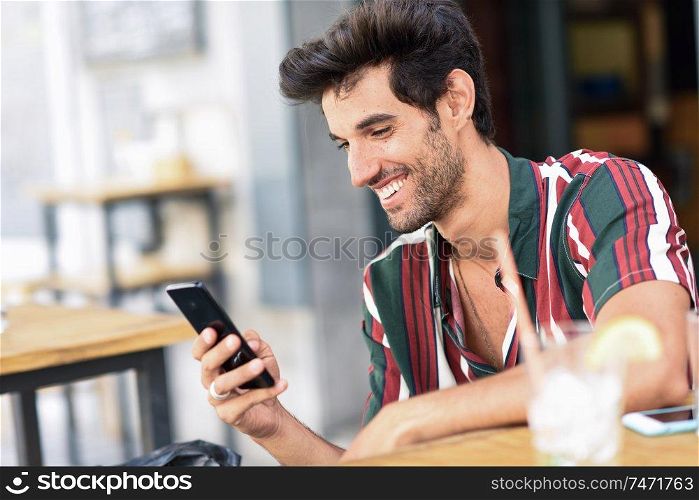 Young man using smartphone in an urban cafe. Male wearing casual clothes.. Young man using smartphone in an urban cafe.