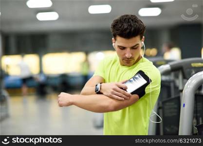 Young man using smartphone standing in the gym before the training. Attractive male with smartwatch